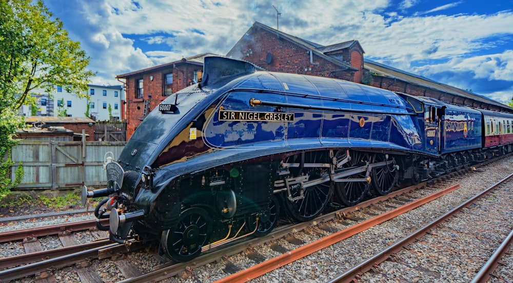 a blue train traveling down train tracks next to a building