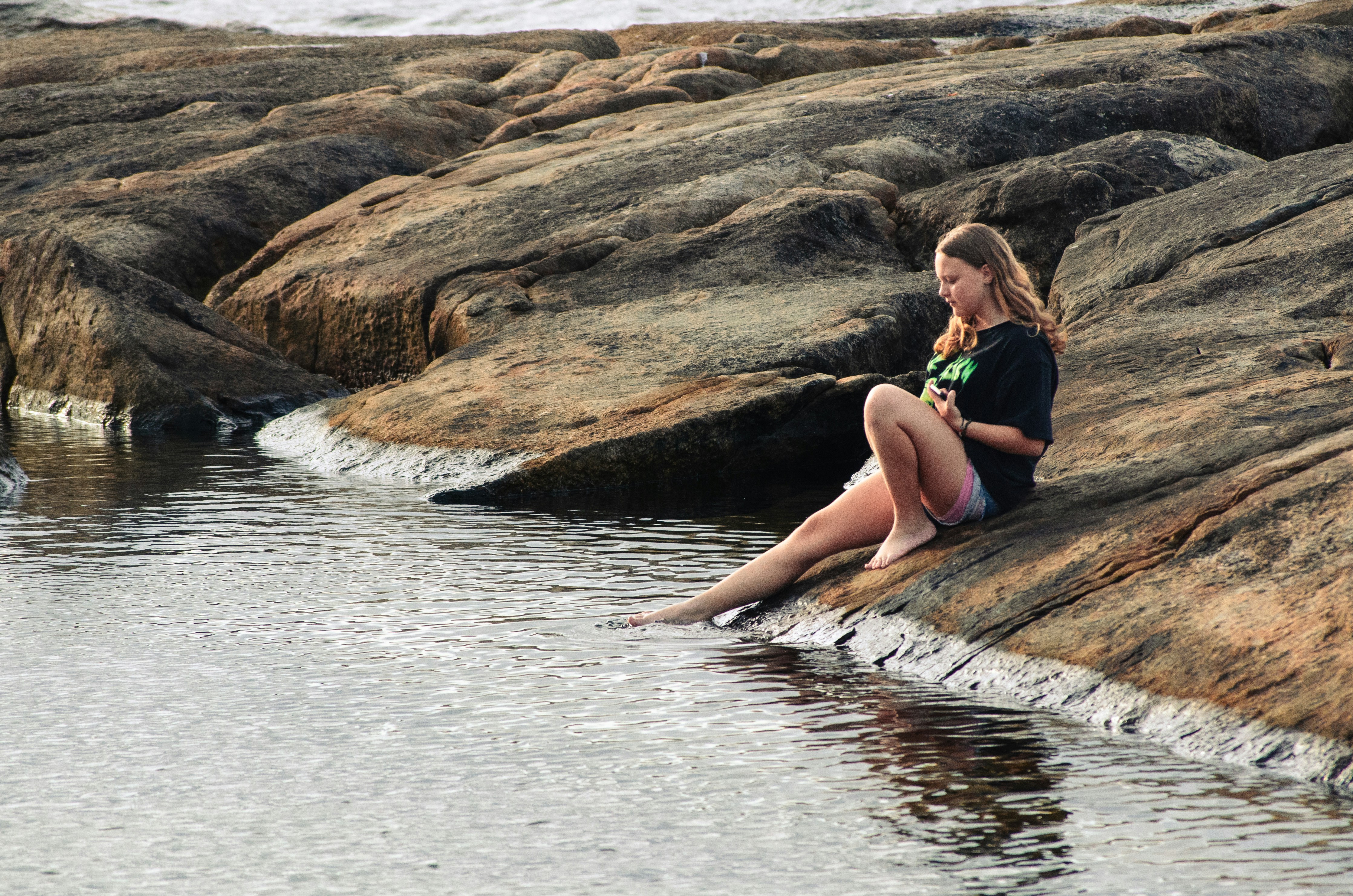 a woman sitting on a rock next to a body of water
