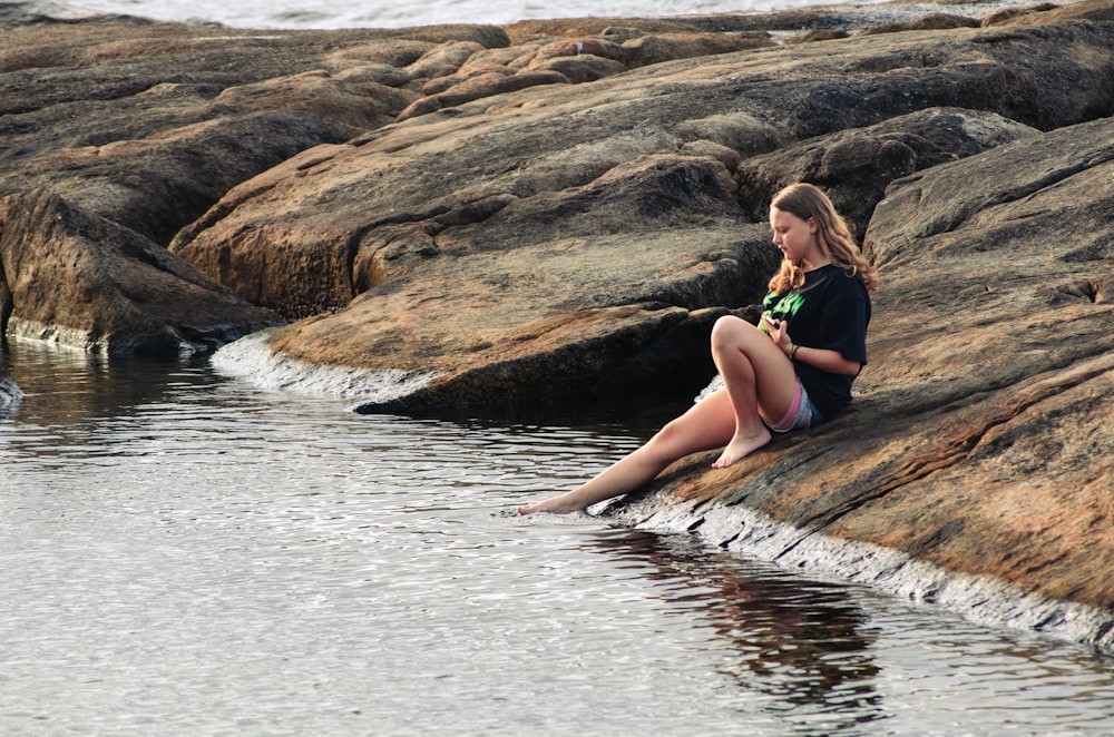 a woman sitting on a rock next to a body of water