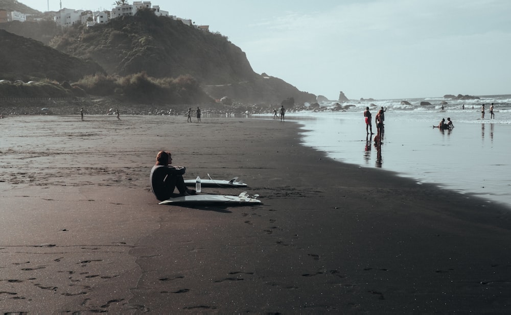 a person sitting on a beach with a surfboard