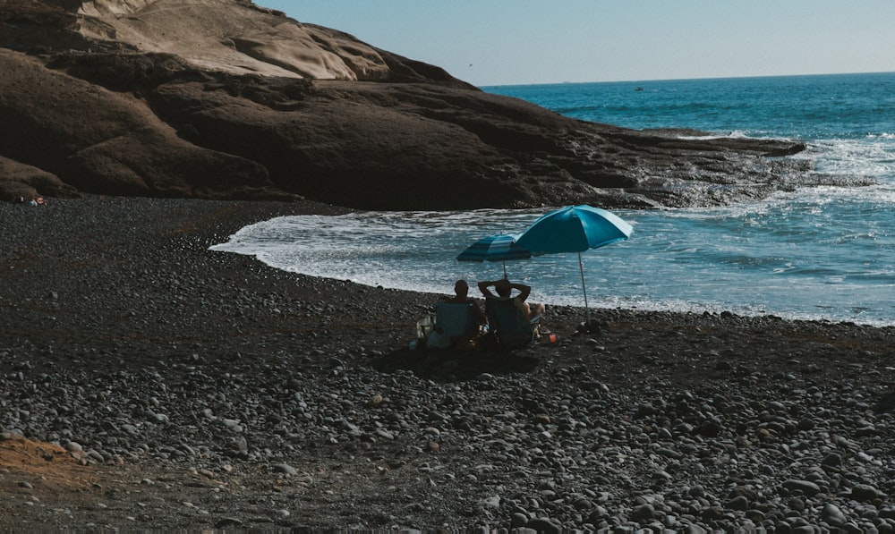 a group of people sitting under an umbrella on a beach