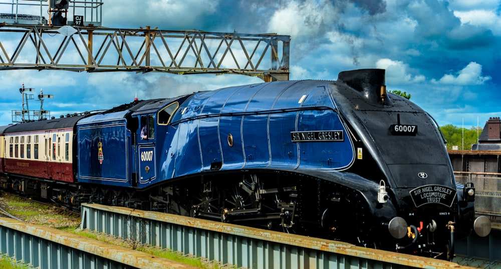 a blue train traveling down train tracks next to a bridge