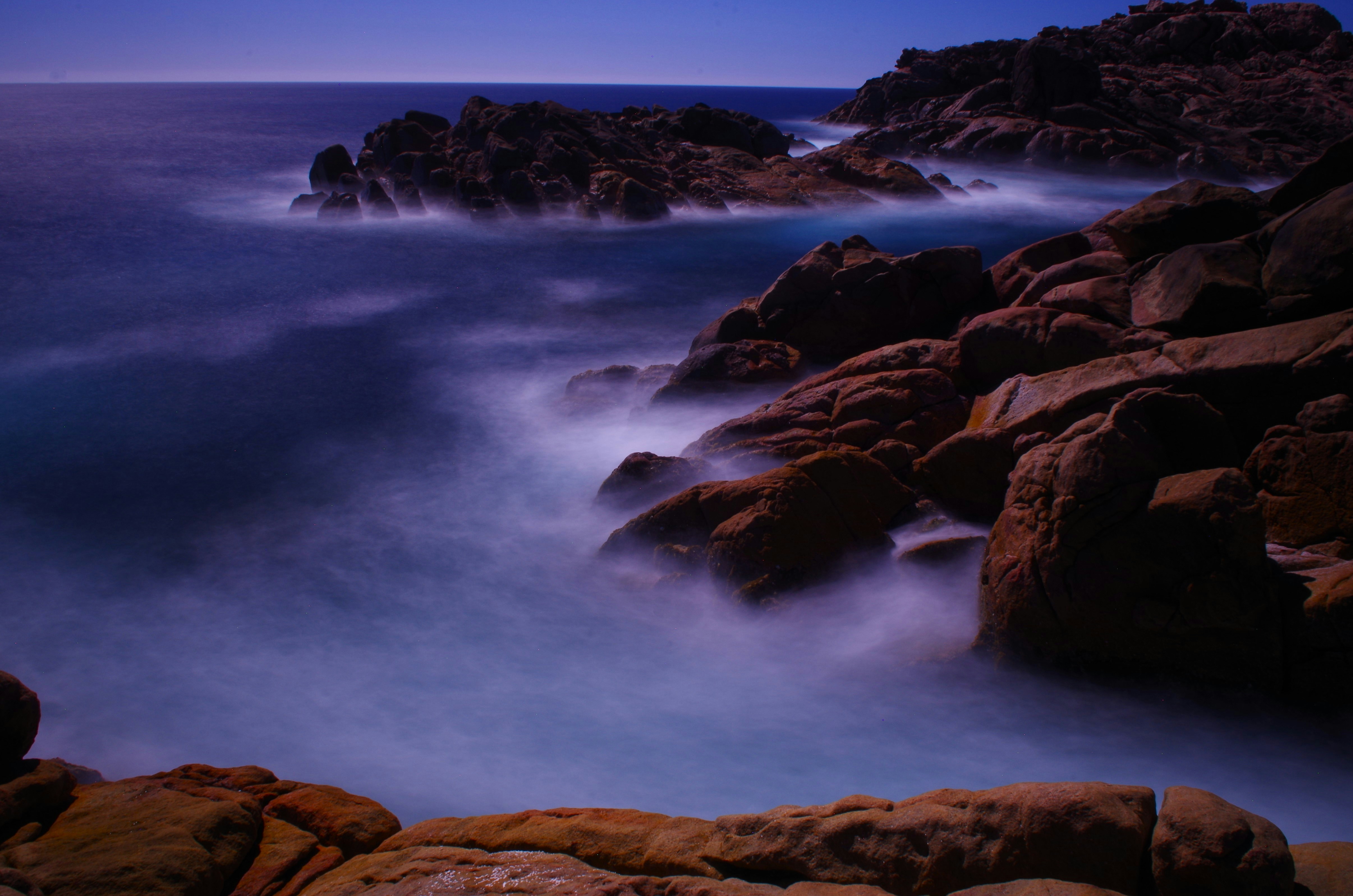 a long exposure photo of the ocean and rocks
