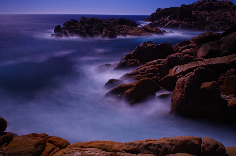 a long exposure photo of the ocean and rocks