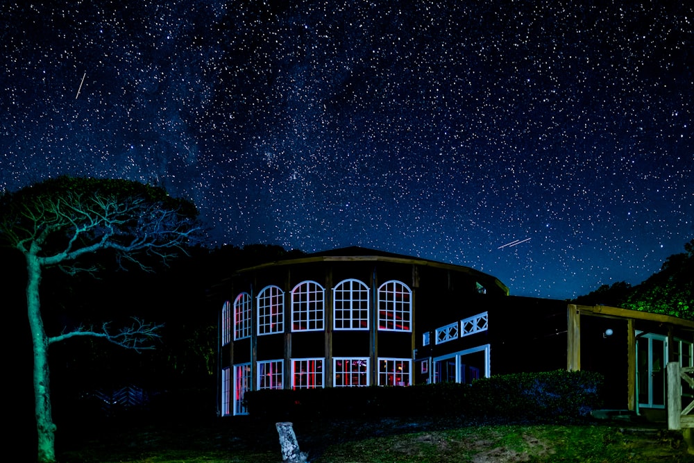 a house with a tree in the foreground and a night sky full of stars