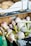 A collection of fresh garlic bulbs with purplish-white skins is displayed in a cardboard box. In the background, there is another box containing round, light brown squashes. The boxes have simple decorative designs on them.