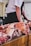 Chunks of raw meat are arranged on a wooden butcher's block. In the background, a person stands wearing a white shirt and dark apron, handling the meat.