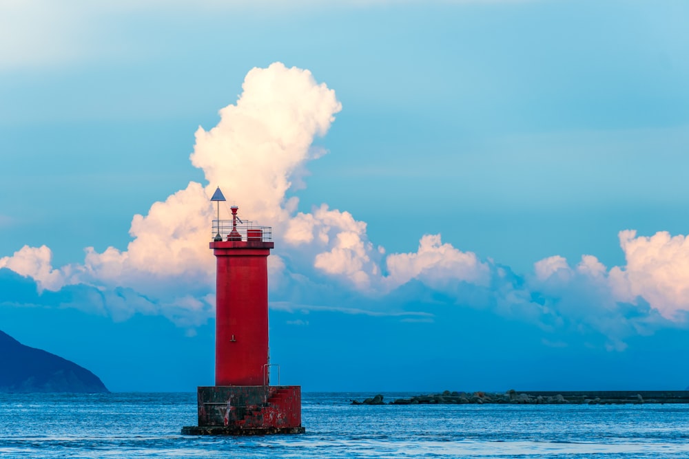 a red light house sitting in the middle of a body of water