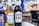 Three bottles of non-alcoholic beverages are arranged on a table in an outdoor setting. The bottles are branded as Erdinger Weissbrau, Thatchers Zero, and Doom Bar Zero. The background features blurred patio furniture and blue umbrellas, suggesting a relaxed and casual environment.