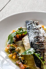 Close-up of a perfectly grilled fish served on a rustic wooden plate with lemon wedges.