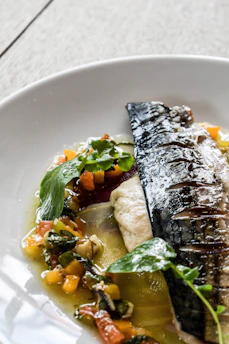 Close-up of a perfectly grilled fish served on a rustic wooden plate with lemon wedges.