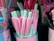 A variety of pastel-colored pens are displayed in a container. The pens are predominantly pink and mint green, with some featuring illustrations of unicorns. The container housing the pens also has pastel designs and unicorn graphics, adding to the whimsical and playful theme.