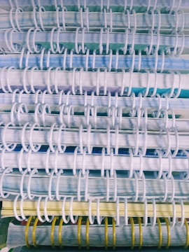 A close-up view of several stacked spiral-bound notebooks, showcasing the binding coils in white and yellow. The pages exhibit a mix of blue, green, and yellow hues.