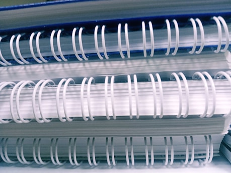Several spiral-bound notebooks are stacked on top of each other, showcasing the loops of white wire binding against the white and blue edges of the covers.