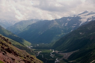 A panoramic view of the Himalayas with lush green valleys and a serene river.