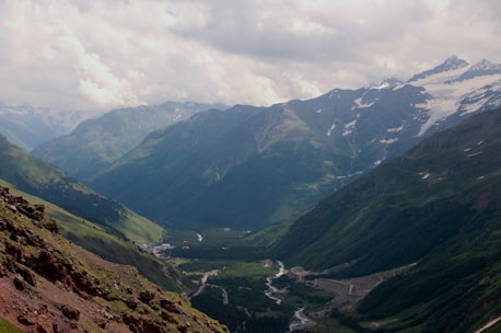 A panoramic view of the Himalayas with lush green valleys and a serene river.