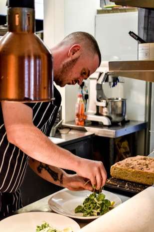 a man in a kitchen preparing food on a plate