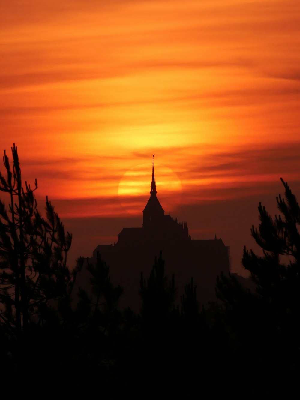 the sun is setting behind a building with a spire