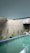 An indoor swimming pool with clear, blue-green water is surrounded by small, potted plants along the perimeter on a light-colored wall. The ceiling is a smooth, muted blue-gray. The poolside features a modern architectural element, including minimalistic design and clean lines.
