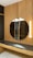 A modern interior features a circular mirror mounted on a vertical wooden panel with a slatted design. Beneath the mirror is a dark countertop with a subtle marbled pattern, supported by a light wooden structure with drawers. Two vertical light fixtures are positioned beside the mirror, providing soft illumination.
