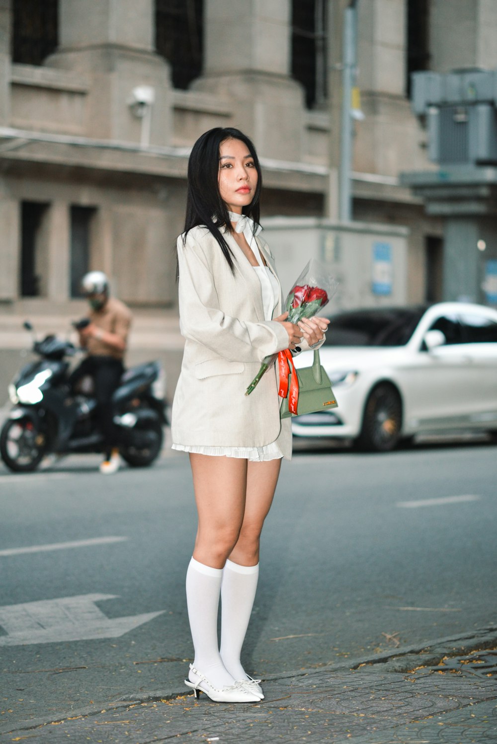 a woman standing on the side of a street holding flowers