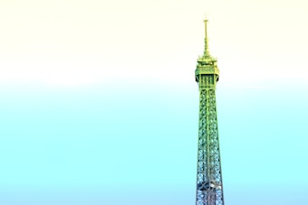 A stylized depiction of the Eiffel Tower dominates the frame, rising against a pastel gradient sky. The structure is infused with shades of green and blue, contrasting with the soft yellow and cyan sky, creating a surreal and artistic effect.