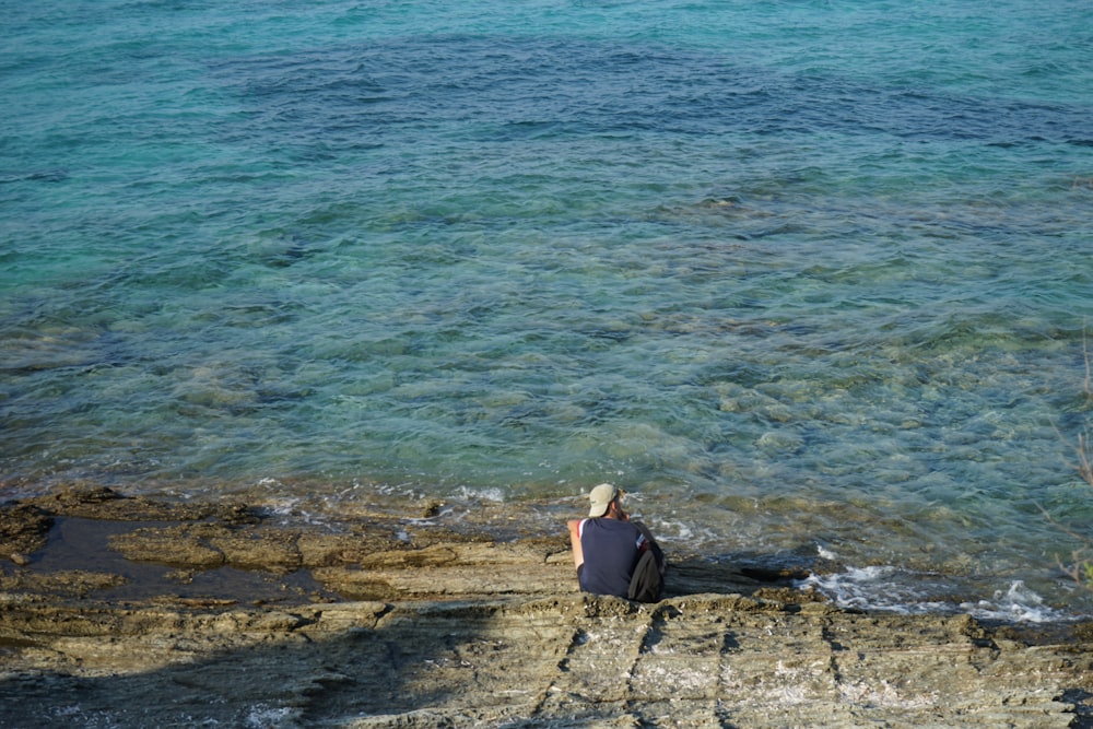 a man sitting on a rock next to the ocean