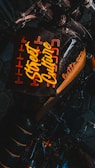 A dark-toned image featuring a motorcycle with a stylized, prominent seat design that includes the text 'Street Culture' in bold, yellow lettering. The words are surrounded by an orange geometric pattern, providing a vibrant contrast against the black background. Part of the motorcycle's handlebar and frame are visible, adding to the urban aesthetic.