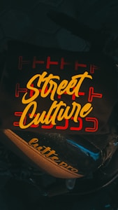 A dark background is overlaid with the bold, yellow cursive text 'Street Culture' featured prominently on a surface. The text is surrounded by red linear designs, adding an urban artistic touch. Below, the words 'lutte pro' are printed on part of a motorbike.