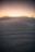 Close-up of smooth desert sand dunes under a warm, glowing sunset sky.