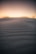 Close-up of smooth desert sand dunes under a warm, glowing sunset sky.