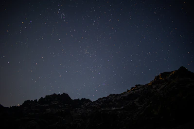 the night sky with stars above a mountain