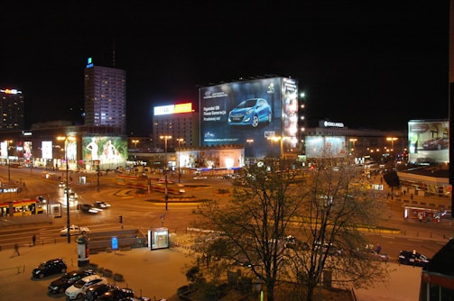 A nighttime cityscape featuring illuminated advertising posters on main roads.