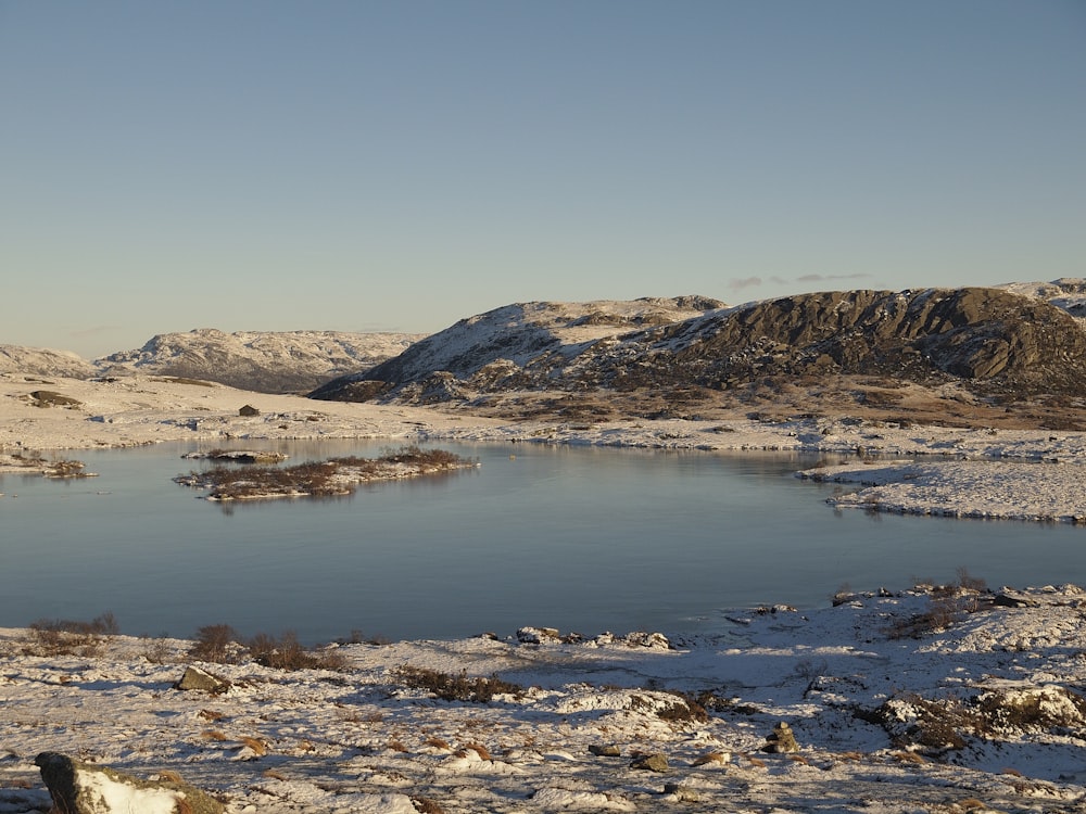 a lake surrounded by snow covered mountains in the middle of winter