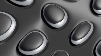 A close-up pattern of convex, oval-shaped structures with smooth surfaces on a dark, glossy background. The elliptical forms have a metallic appearance and are arranged in a repetitive, uniform manner.
