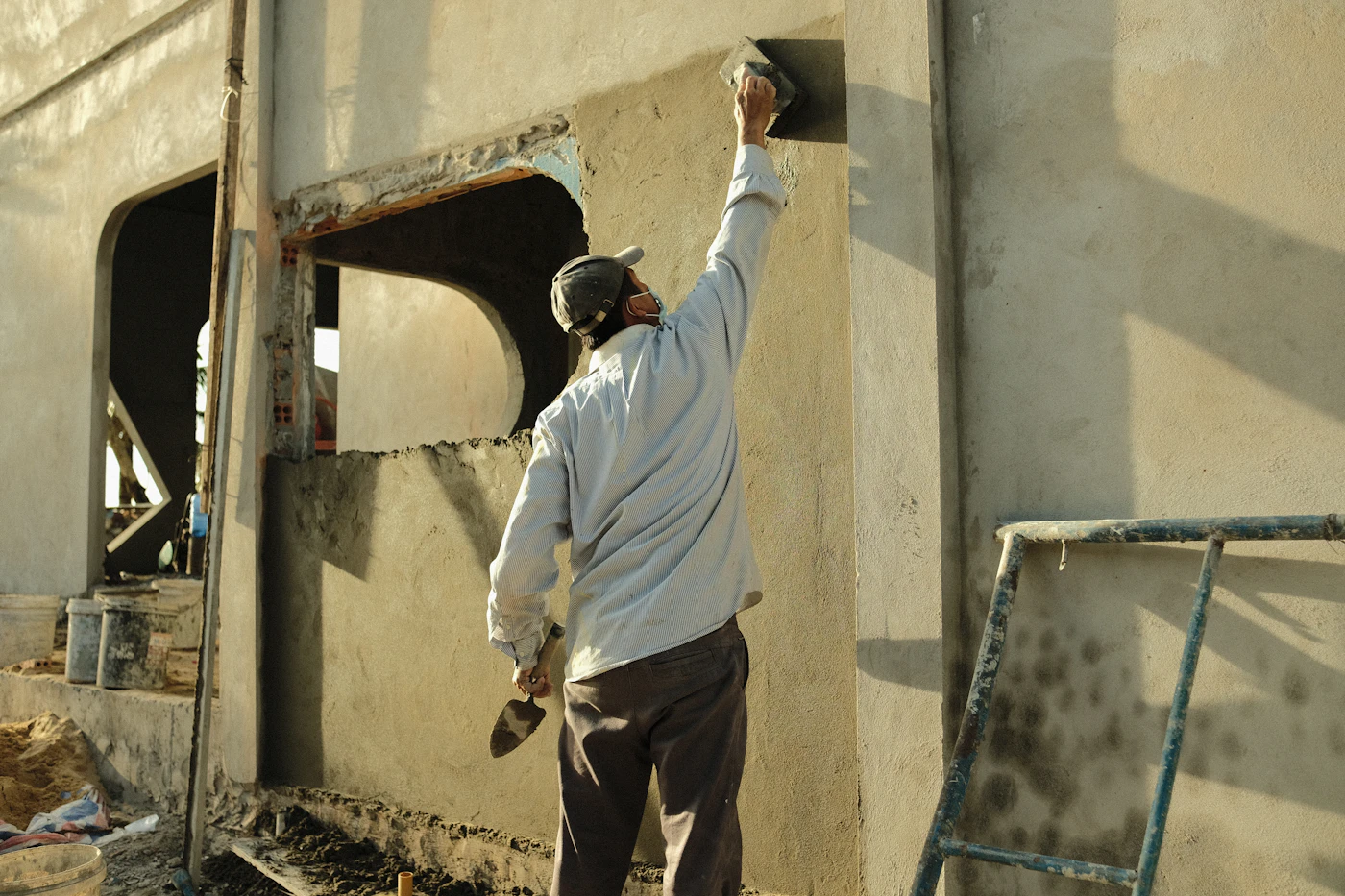 Artisan avec un marteau devant une façade en travaux
