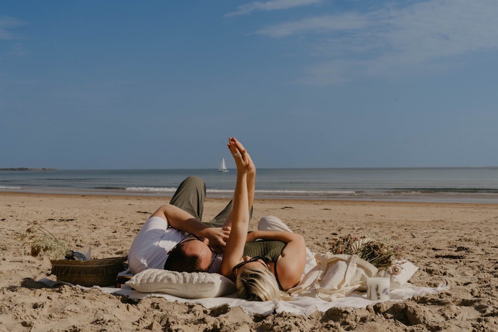 a man and woman laying on a blanket on the beach