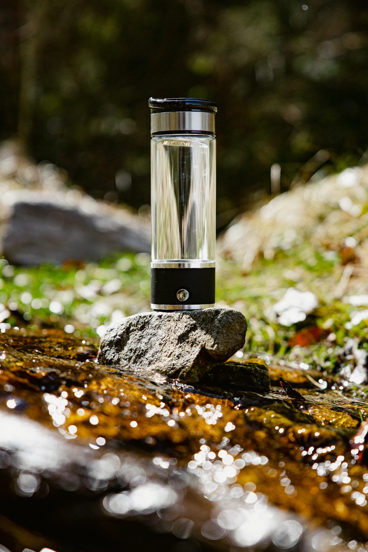 Glass water bottle displayed on a rock by a stream