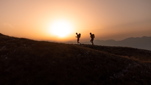 Sunset casting warm light over Mount Etna, with silhouettes of hikers in the foreground.