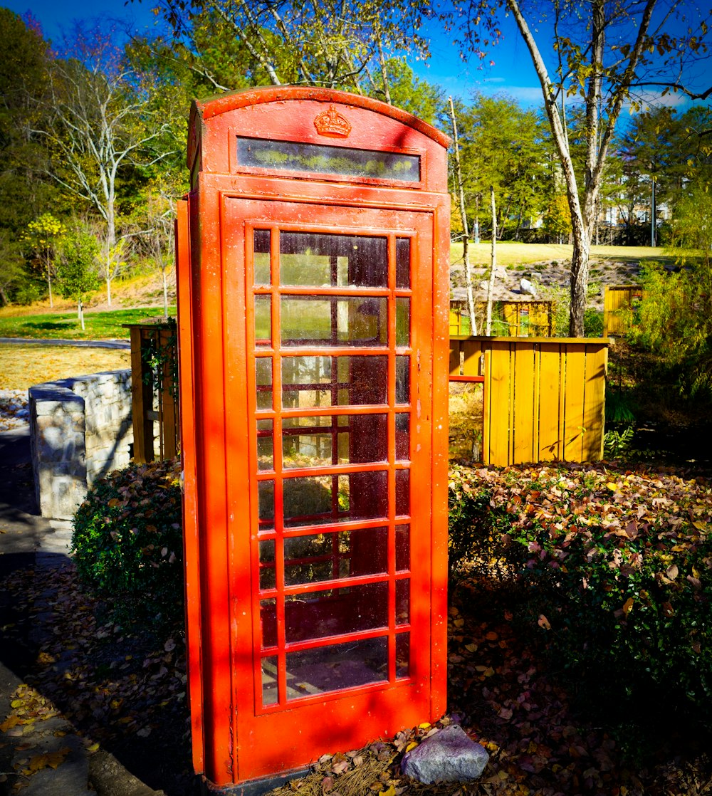 a red phone booth sitting next to a bush