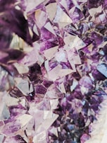 A close-up view of a cluster of amethyst crystals, showcasing the natural beauty of the geometric formations. The varied shades of purple and lavender create a striking and vibrant visual pattern.