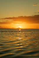 the sun is setting over the ocean with a boat in the distance