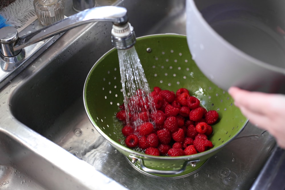 a person is washing raspberries in a sink