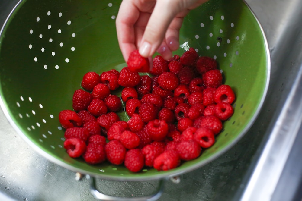 a person picking raspberries from a strainer