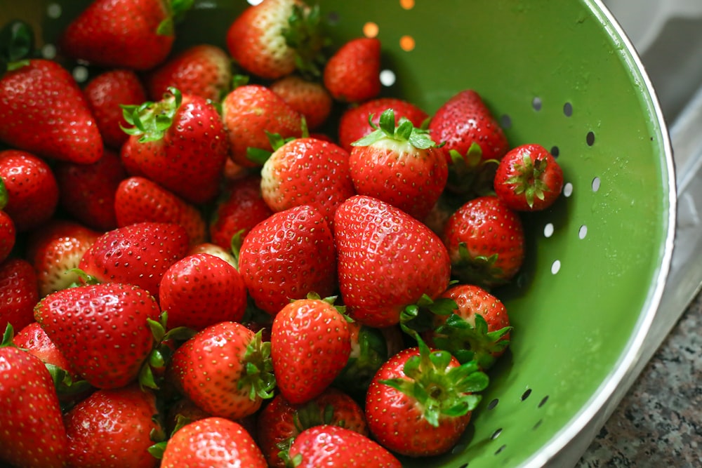 a green bowl filled with lots of ripe strawberries