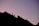 Silhouettes of two people climbing a jagged mountain ridge against a backdrop of a softly colored sky at dawn or dusk.