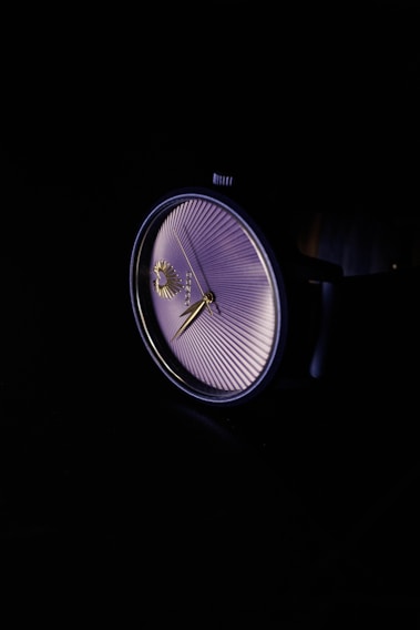 Close-up of a luxury watch dial with intricate details and polished hands against a dark background.