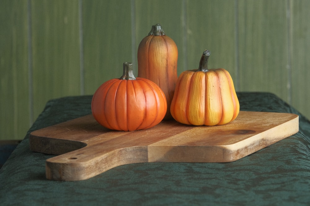 three pumpkins are sitting on a cutting board