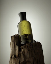 A sleek bottle of Louvel spirit resting on a natural wooden surface, surrounded by soft shadows and hints of forest greenery.