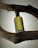 A bottle of Hugo Boss perfume is balanced horizontally between two dark, textured tree branches. The bottle is translucent with a greenish hue, and the branding is clearly visible on its surface. The background is a soft gradient, enhancing the earthy and natural contrast of the setup.